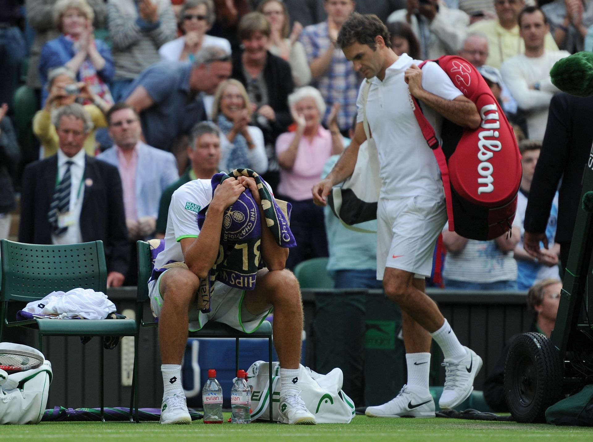 Sergiy Stakhovsky sits with his head covered as Roger Federer walks by his side. (Source: Getty)